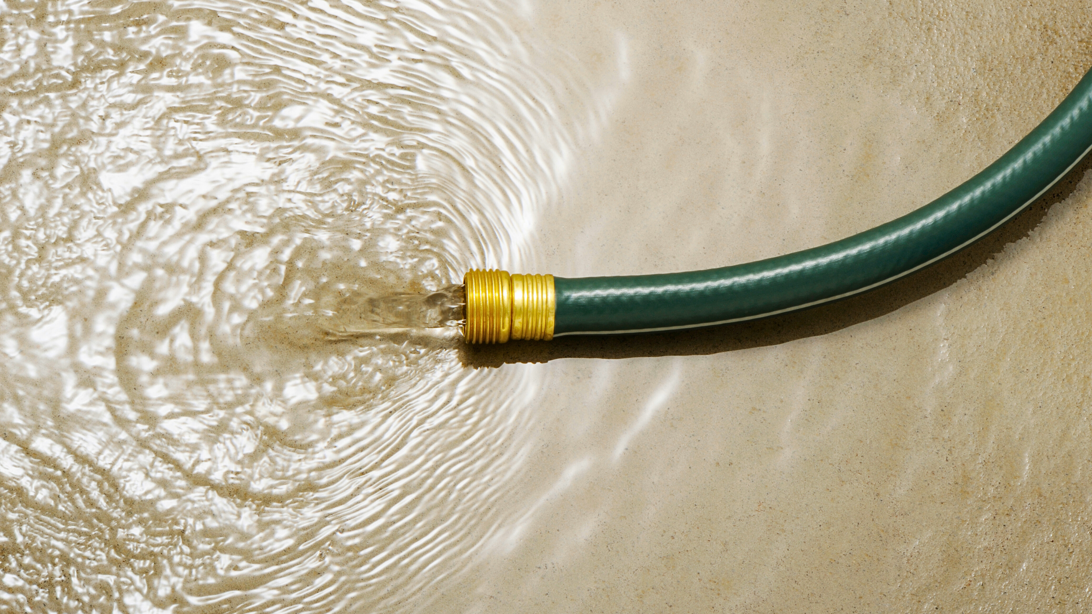 A garden hose left running on concrete, forming a large pool of wasted water.