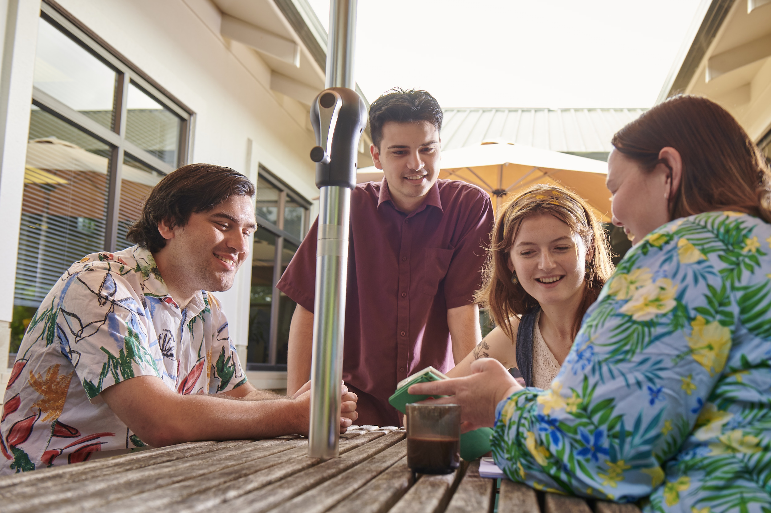 Four young people surrounding a picnic table, smiling and looking at a phone screen