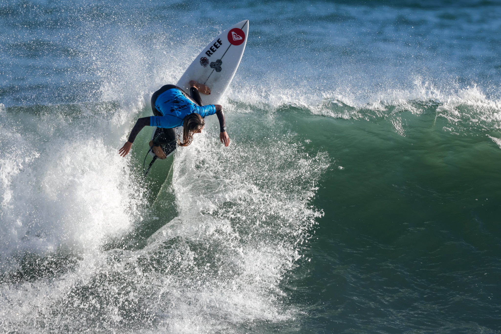 Surfer in a blue rash guard performing a sharp turn on a wave with water splashing around.
