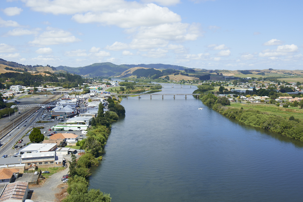 Aerial view of Huntly showing the Waikato River, bridges, township, and surrounding hills on a sunny day.