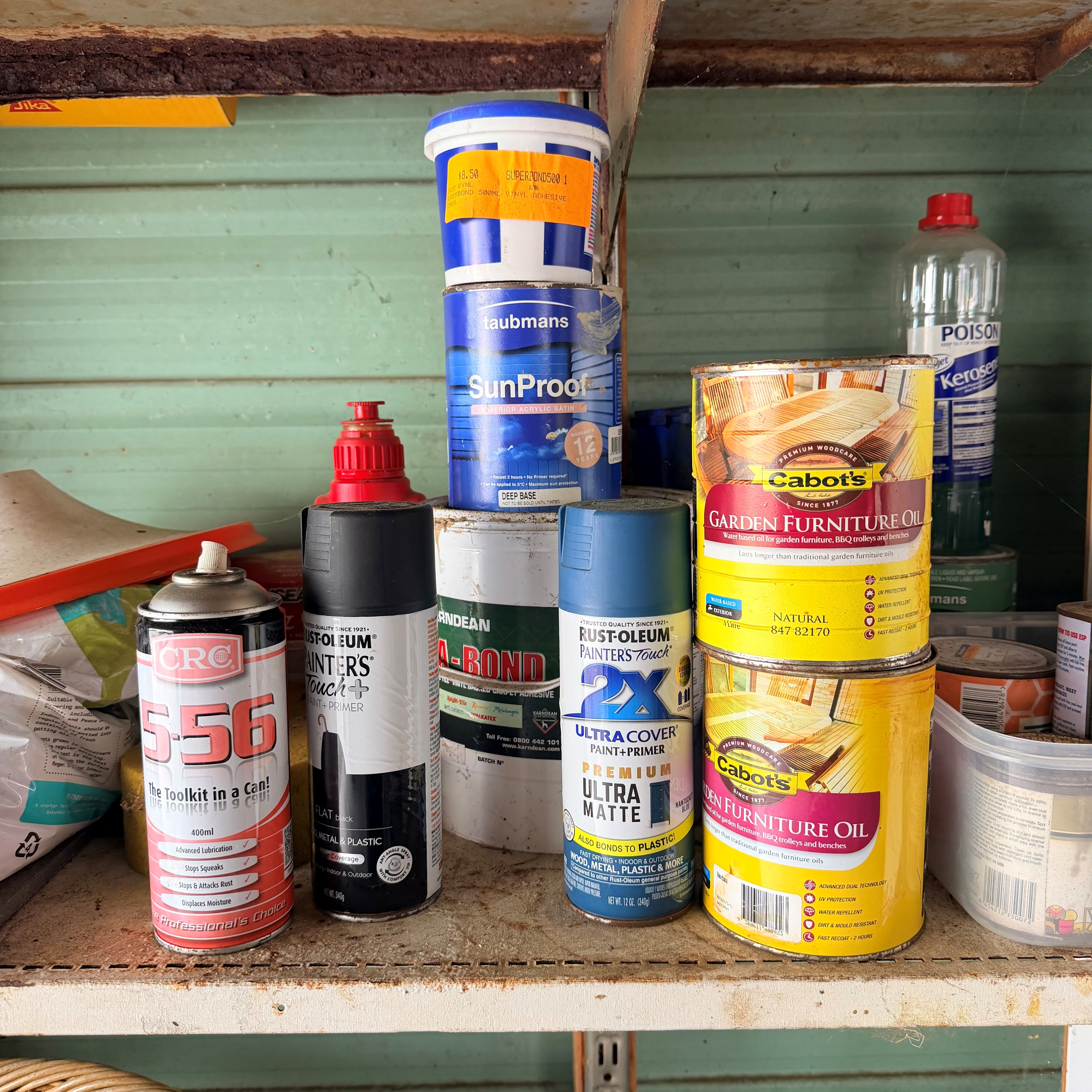 A cluttered shelf with various paint and oil cans, including brands like Cabot’s and Rust-Oleum. The setting appears like a garage or a workshop.