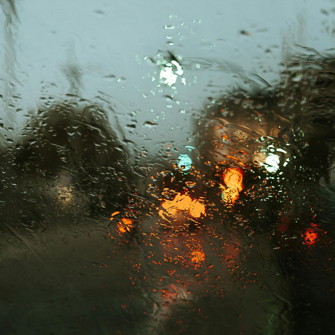 Blurry view through a rain-streaked window, with colorful, out-of-focus lights in orange and teal