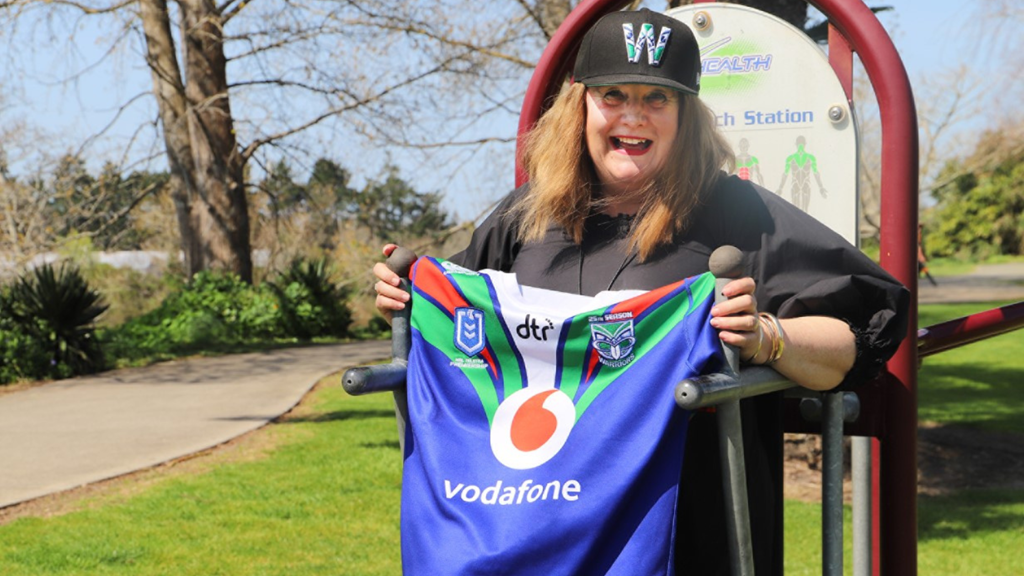 Mayor Jacquie smiling wearing a Warriors cap while holding a Warriors t-shirt outside on a sunny day.