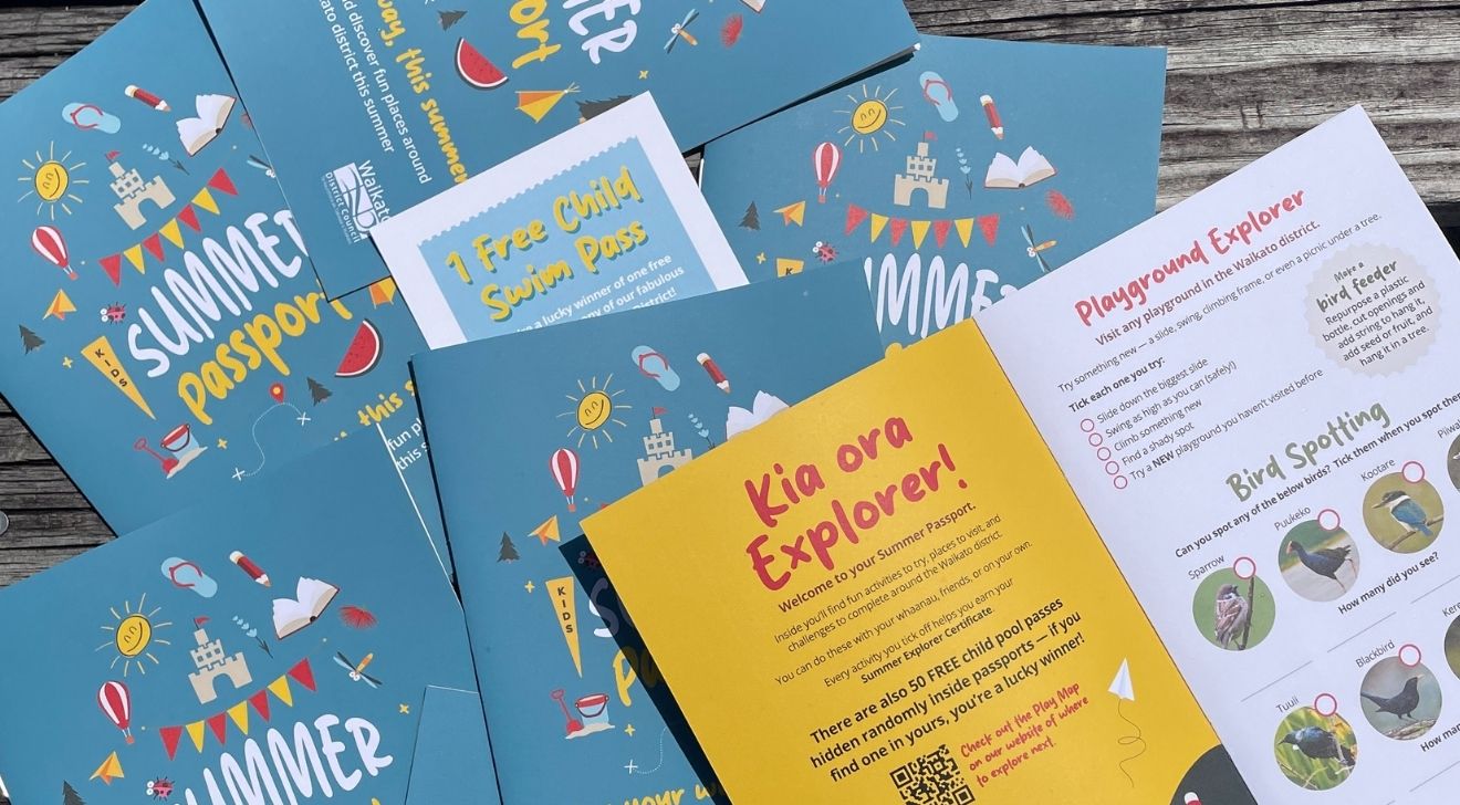 Colorful brochures titled 'Summer Passport' with playful illustrations of sandcastles, balloons, and kites on a wooden surface. A yellow insert reads 'Kia ora Explorer!' offering activities and a '1 Free Child Swim Pass.'