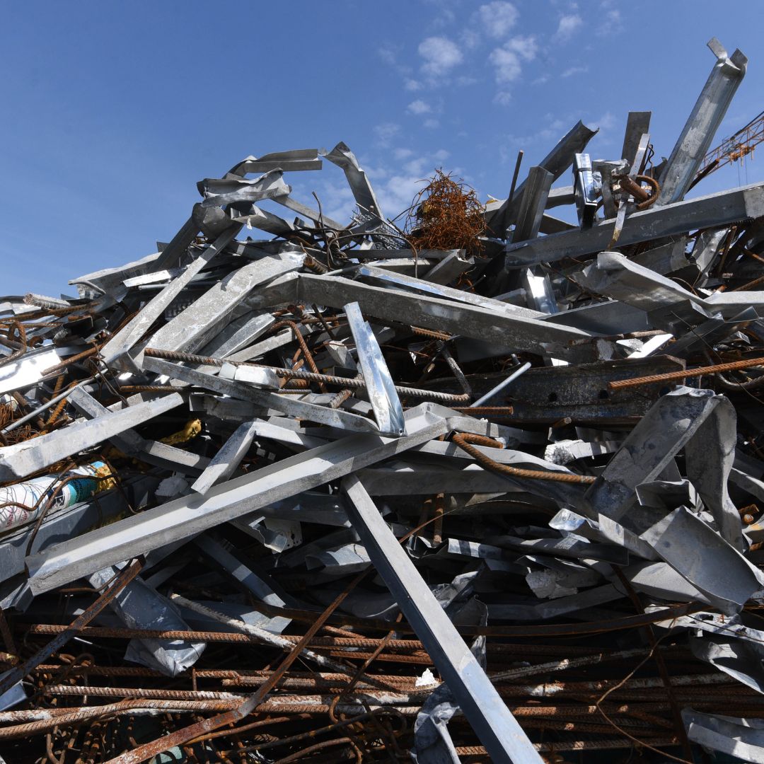 A pile of twisted metal scraps and rusty iron rods against a clear blue sky, conveying a sense of chaotic industrial waste and recycling.