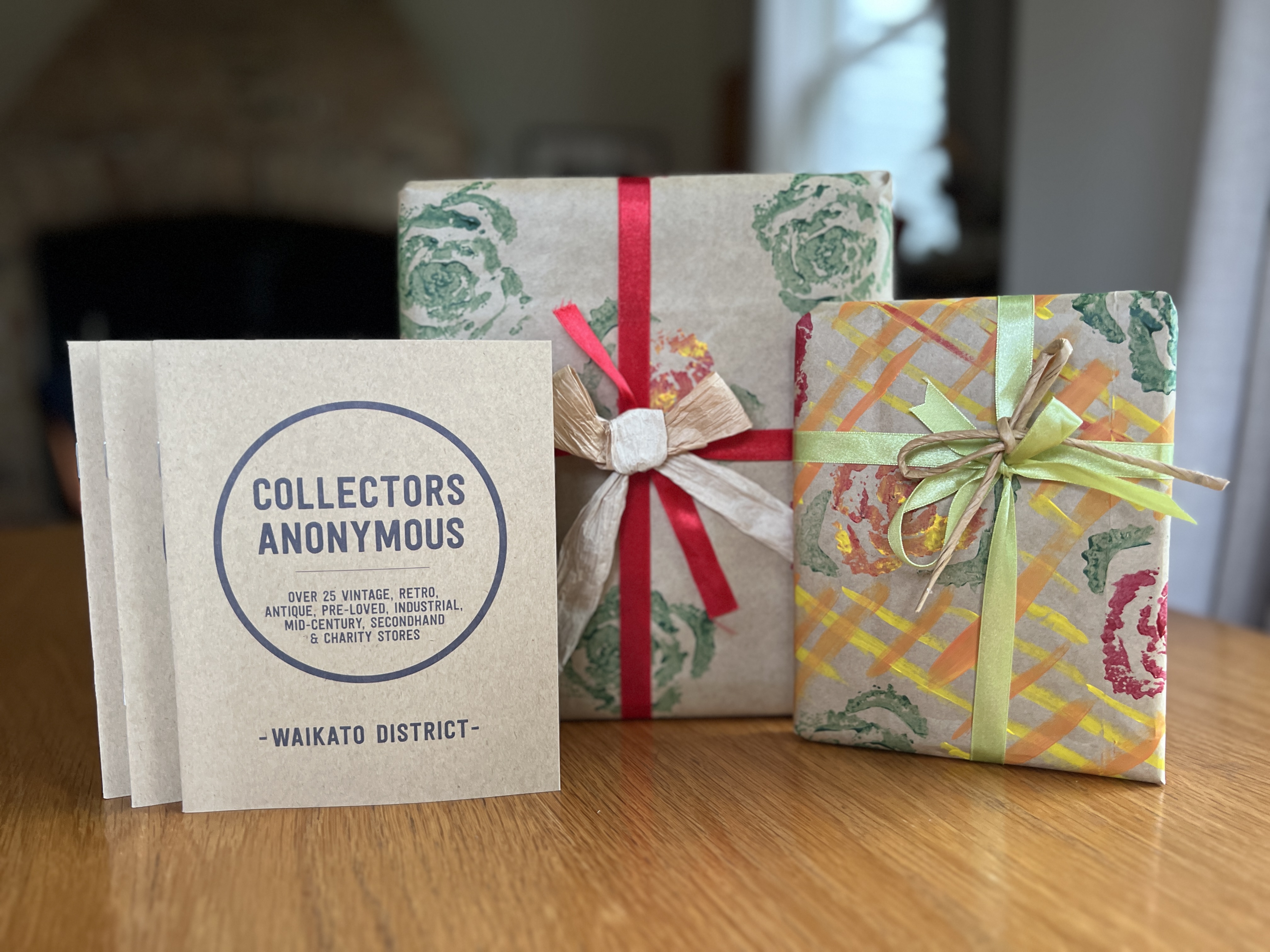 Three gifts wrapped in floral paper with colorful bows sit on a table beside a "Collectors Anonymous" flyer, creating a festive and inviting scene.